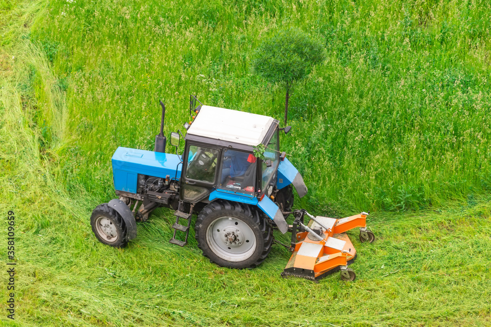 Tractor uses trailed lawn mower to mow grass on city lawns, aerial view. Tractor uses trailed lawn mower to mow grass on city lawns, aerial view.