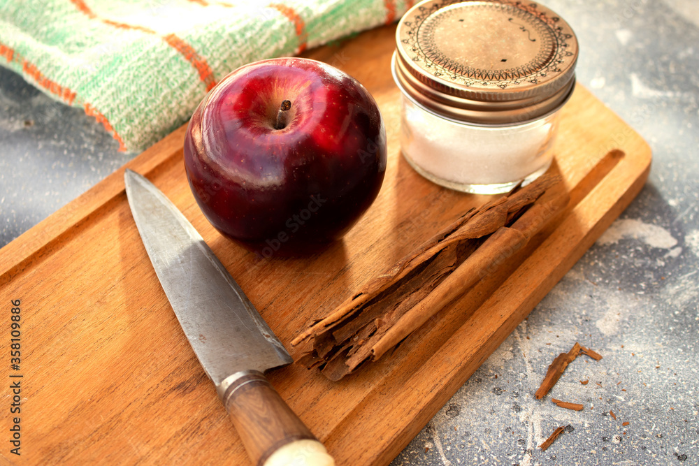red apple, cinnamon stick and sugar on a wooden board and a knife with rustic background red apple, cinnamon stick and sugar on a wooden board and a knife with rustic background