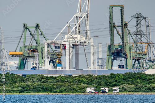 Oostvoorne, The Netherlands, June 14, 2020: three campers by the shore of lake Oostvoornse meer with the industry of the port of Rotterdam in the background photo