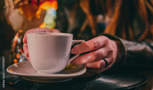 woman hands holding a white cup of tea or coffee standing on the table in cafe