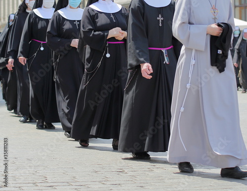  Nuns walk in line in street, some with protective face mask