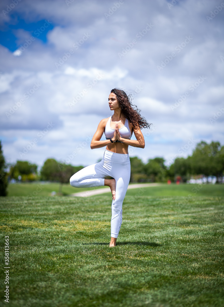 Young pretty fitness woman doing yoga postures in a park on the grass with white clothes