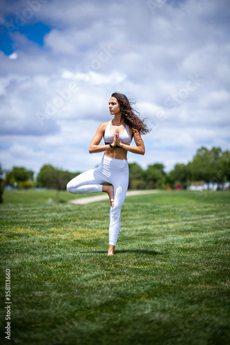 Young pretty fitness woman doing yoga postures in a park on the grass with white clothes