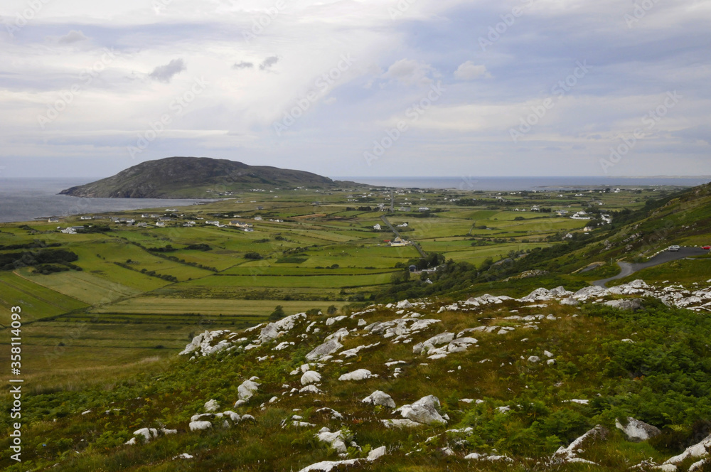 Vue panoramique sur la côte nord irlandaise, ses champs, ses collines, ses rochers et son ciel nuageux, depuis une route au sommet d'un col.