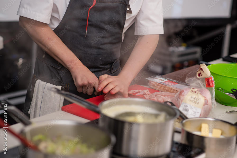 Chef chops meat and prepares meal beside boiling pans Chef chops meat and prepares meal beside boiling pans