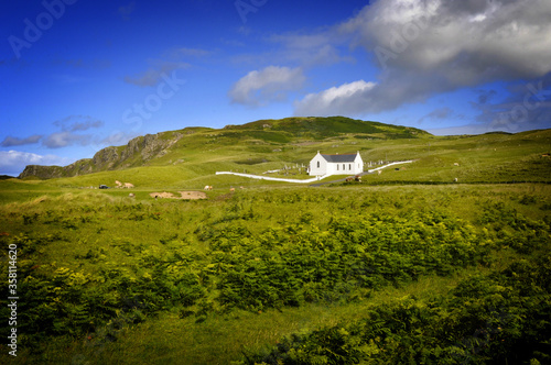 Vue pittoresque sur une petite chapelle blanche au beau milieu de collines verdoyantes sur fond de ciel bleu en Irlande du nord. photo