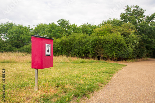A red bin for dog excrement sits beside a footpath in a rural country park
