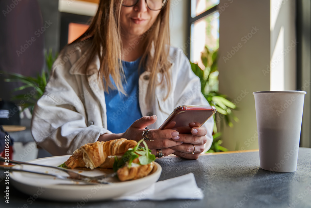 Woman typing text message on smart phone in a cafe. Cropped image of young woman sitting at a table with a coffee using mobile phone. Toned. Selective focus.