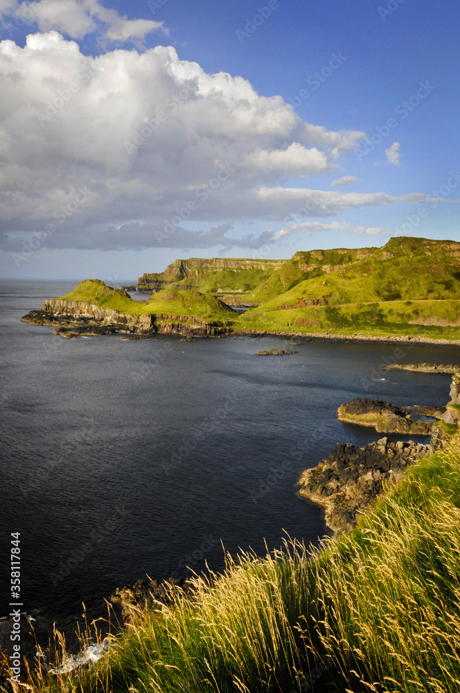 Magnifique vue sur des falaises vertes et verdoyantes contrastant avec le bleu du ciel et de la mer, au soleil couchant, en Irlande du nord.