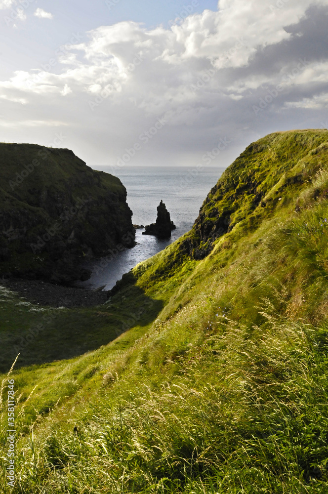 Vue sur un piton rocheux se dressant au milieu d'un crique faite de falaises recouverte de gazon vert, au bord de la mer, en Irlande du Nord.