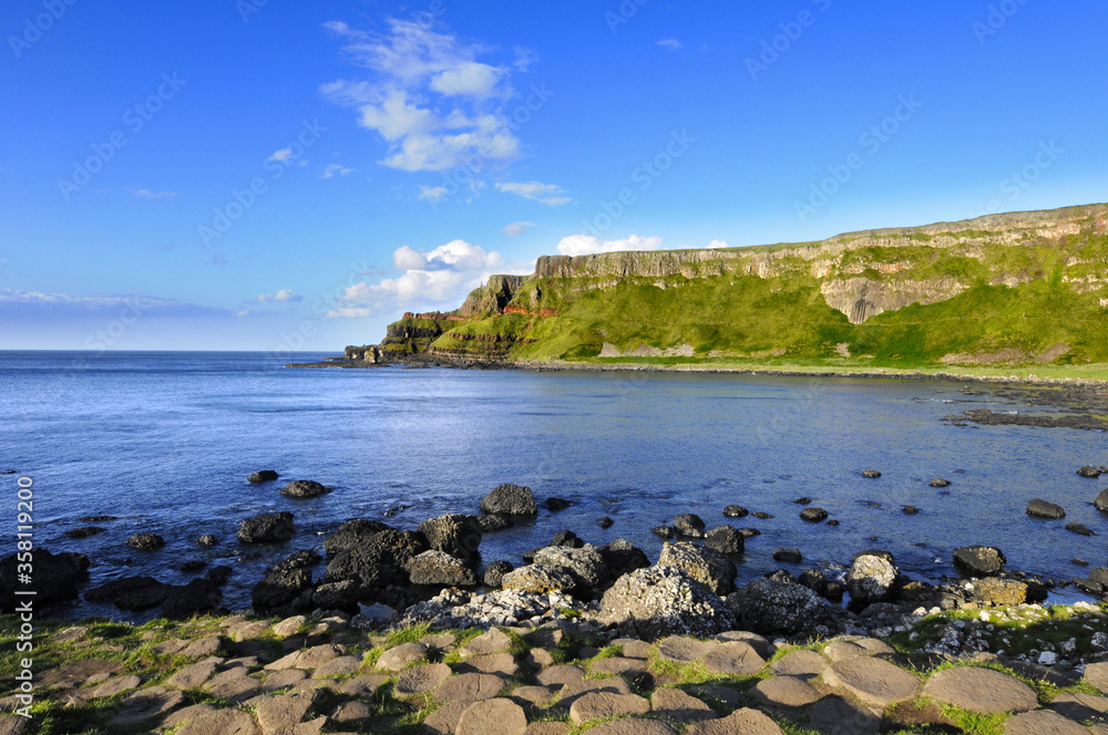 Obraz premium Magnifique vue sur des falaises vertes et verdoyantes contrastant avec le bleu du ciel et de la mer, au soleil couchant, en Irlande du nord.
