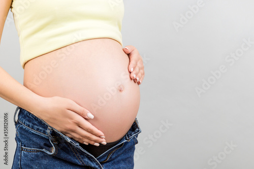 Close up of pregnant woman in unzipped jeans showing her naked belly at colorful background with copy space. Baby expecting concept © sosiukin