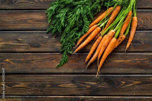 Bunch of fresh carrots with green tops form above copy space