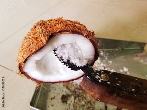 Grating coconut with the help of wooden coconut grater