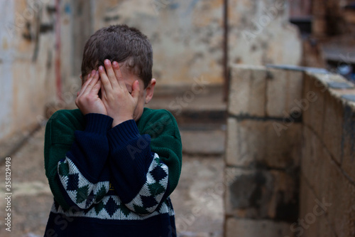 a poor Syrian child in slum covering his face with his hands, sneak peaking in between