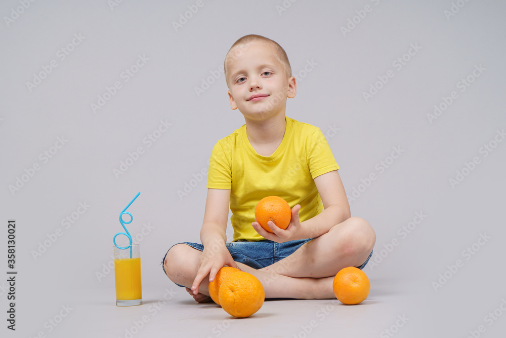 Smiling boy sitting with fruit orange and drink. Isolated on gray Smiling boy sitting with fruit orange and drink. Isolated on gray