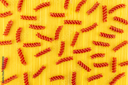 A red spiral pasta lying on a yellow background made of long yellow spaghetti pasta, top view.