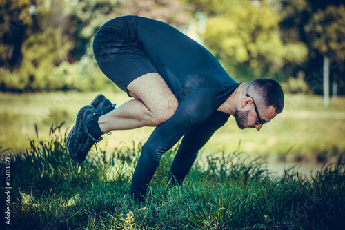 Man stretching hands and legs on green grass in park. Athlete do workout outdoors. Sport, yoga, pilates, fitness, healthy lifestyle concept.