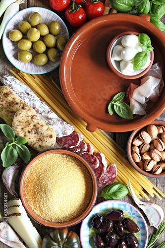 Italian dinner table concept with salami, vegetables variety, pasta, polenta, cheese, nuts and herbs. Ingredients for cooking of traditional mediterranean dinner or lunch. Overhead view