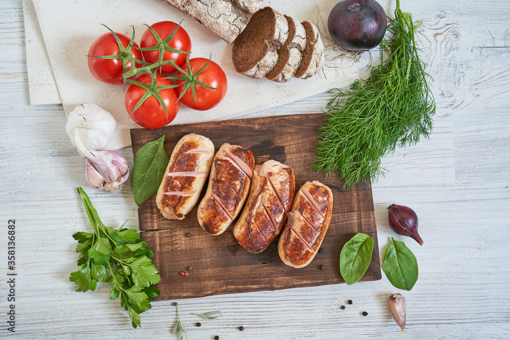 grilled sausages with tomatoes and herbs on the board on white table
