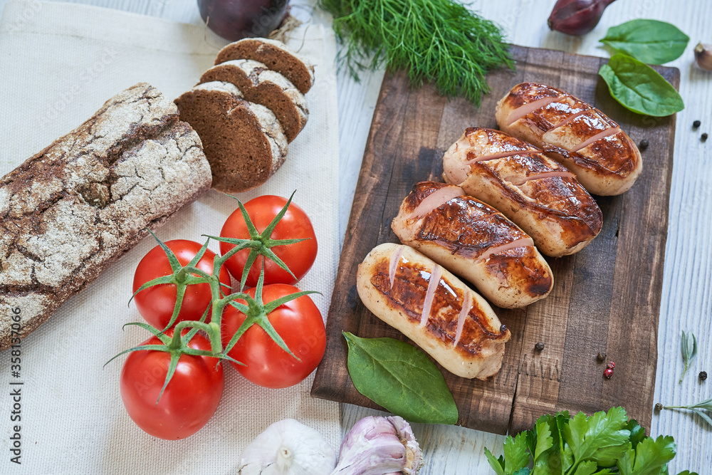 grilled sausages with tomatoes and herbs on the board on white table
