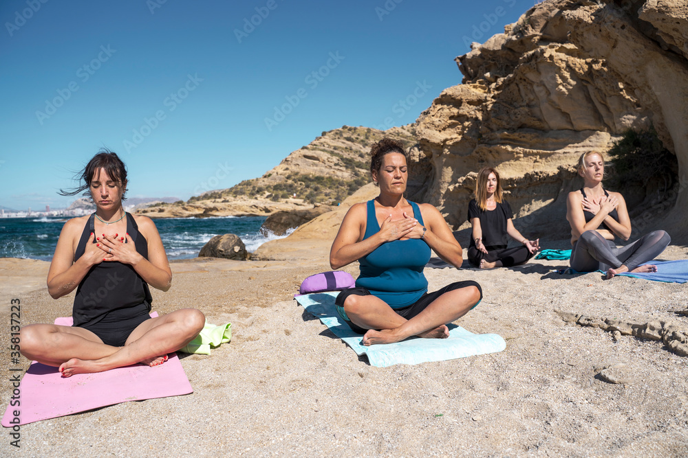 Group of several people practicing yoga and meditation on a beach in sunny day. The group is made up of several men and women of different ages.