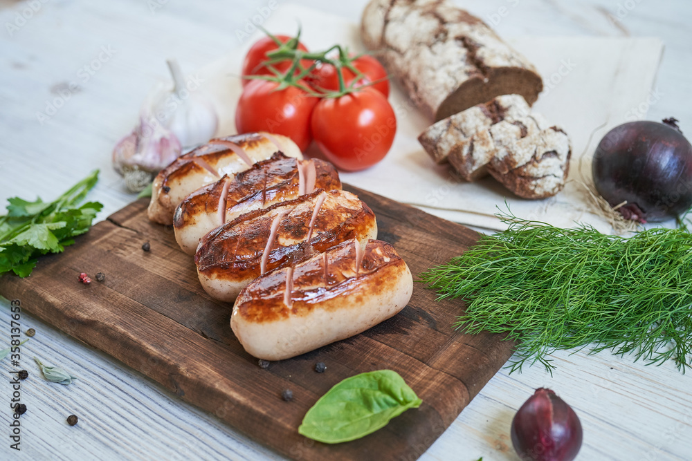 grilled sausages with tomatoes and herbs on the board on white table