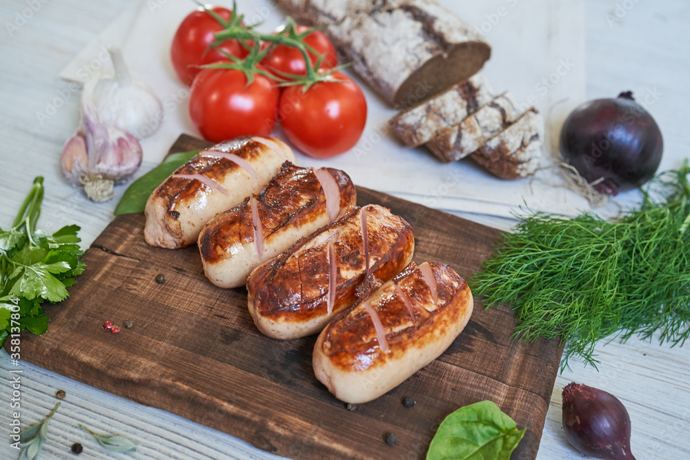 grilled sausages with tomatoes and herbs on the board on white table