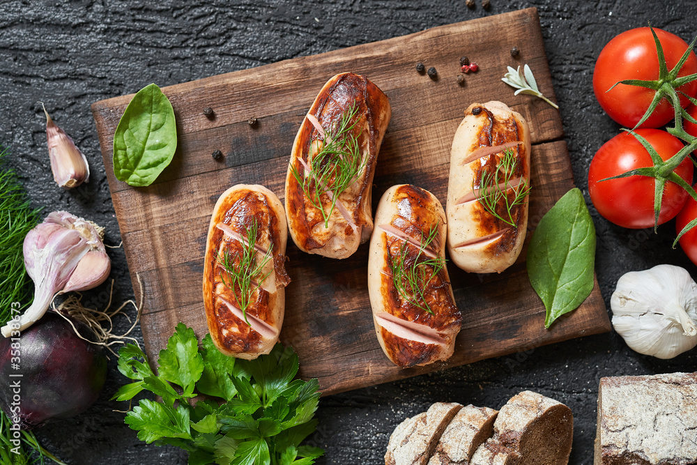 grilled sausages with tomatoes and herbs on the board on a wooden table
