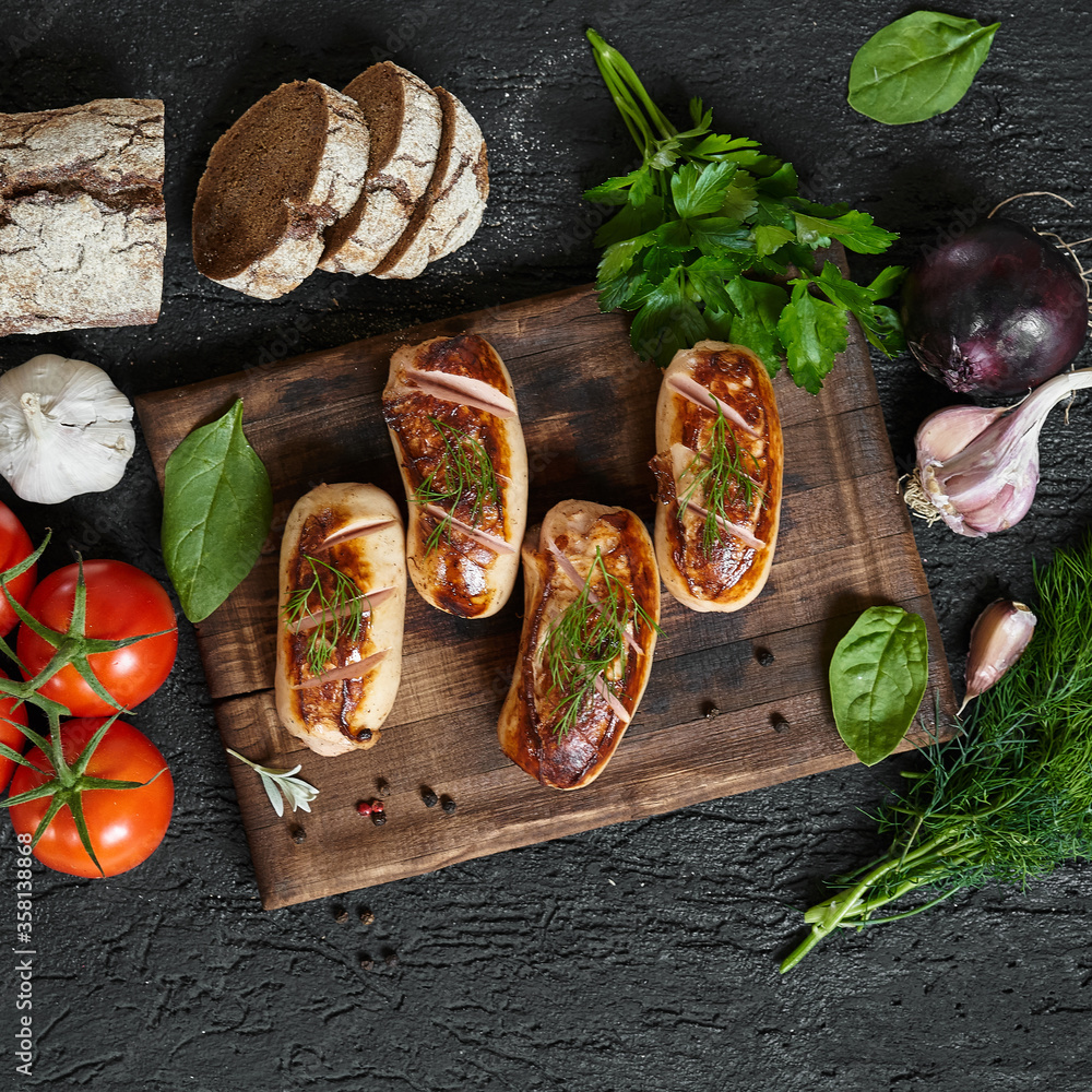 grilled sausages with tomatoes and herbs on the board on a wooden table