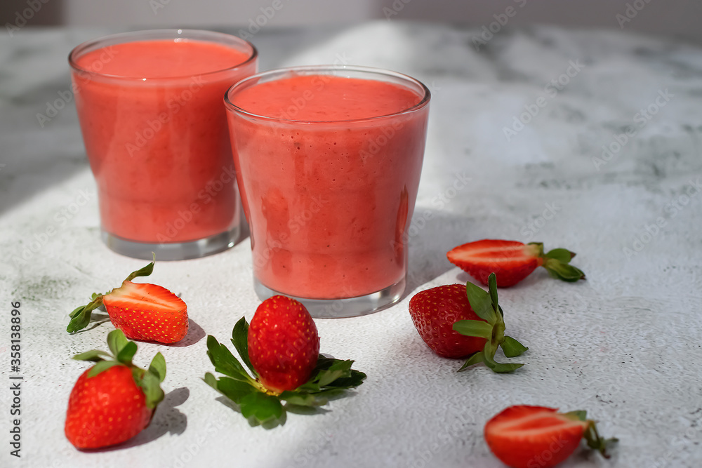 Organic strawberry smoothies in glass cups and ripe strawberries on gray cement background. Organic strawberry smoothies in glass cups and ripe strawberries on gray cement background.