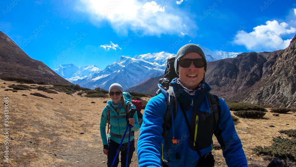 Couple trekking in the Manang Valley, Annapurna Circus Trek, Himalayas, Nepal, with the view on Annapurna Chain and Gangapurna. Dry and desolated landscape.  High snow capped mountain peaks. Happiness