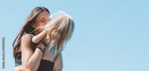 Young fit woman mom with little cute girl on blue sky background, banner © Galina Zhigalova
