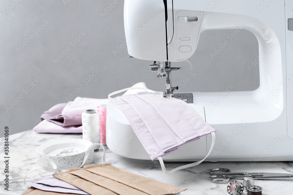 Sewing machine, homemade protective masks and craft accessories on white marble table