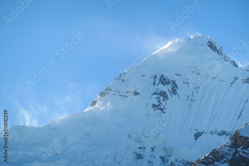 Close up view on powder snow covered Himalayas along Annapurna Circuit Trek, Nepal. Harsh and barren landscape around. Clear and blue sky. High Himalayan ranges in the back. Snow capped mountains