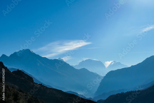 Himalayan chains shrouded in fog  seen from Thorung Phedi  Annapurna Circuit Trek  Nepal. There are multiple mountain chains. Sunbeams breaching through the peaks. Golden hour. Meditation and serenity
