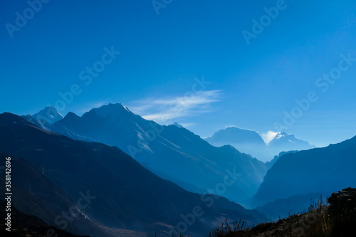 Himalayan chains shrouded in fog, seen from Thorung Phedi, Annapurna Circuit Trek, Nepal. There are multiple mountain chains. Sunbeams breaching through the peaks. Golden hour. Meditation and serenity photo