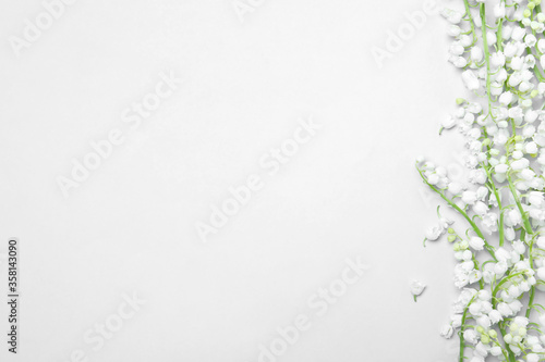 Beautiful lily of the valley flowers on light grey background  flat lay. Space for text