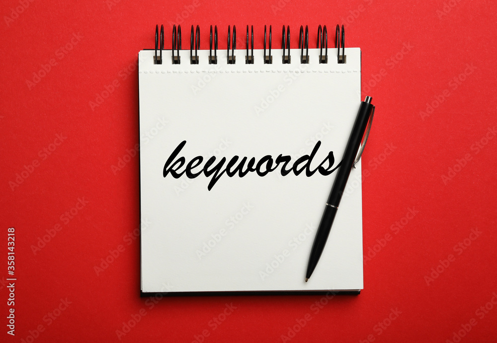 Stylish notebook with text KEYWORDS and pen on red background, top view Stylish notebook with text KEYWORDS and pen on red background, top view