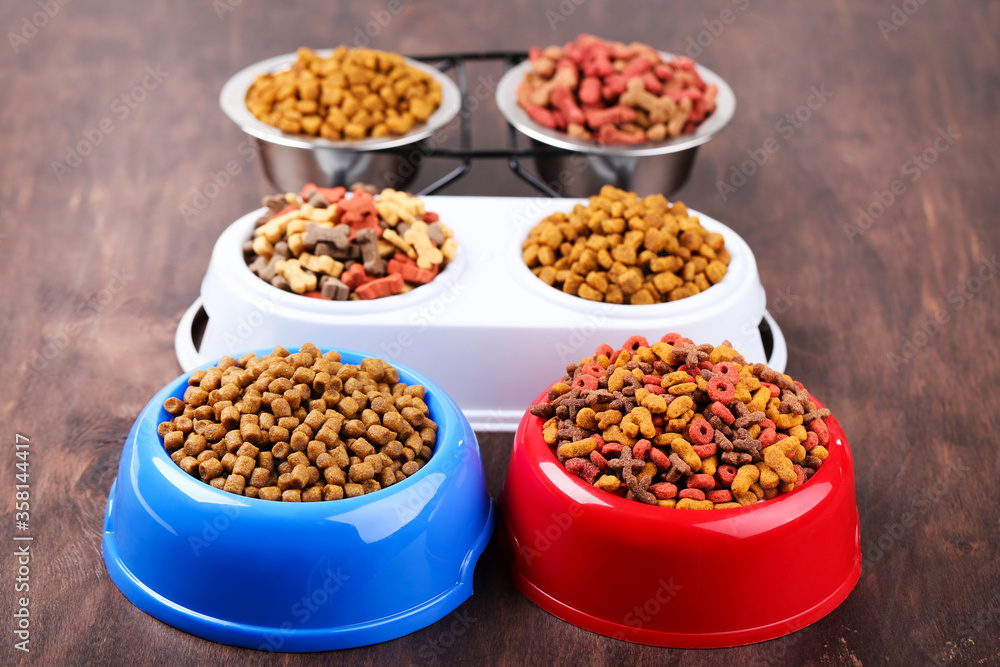 Dry pet food in bowls on brown wooden table Dry pet food in bowls on brown wooden table