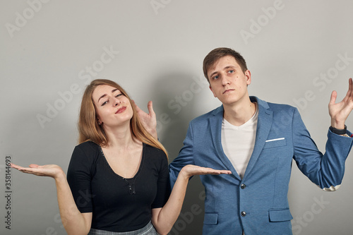 Palms up, place your product here, raising arms wide spread is catching something. Young attractive couple boyfriend girlfriend two people, dressed black t-shirt, blue jacket, grey background