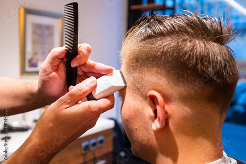 Barber trims the hair of young man with a razor