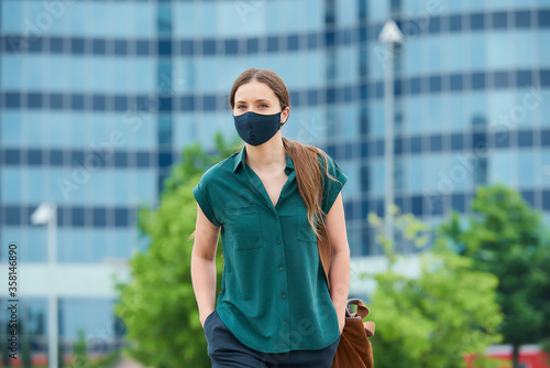 A woman in a medical face mask to avoid the spread of coronavirus walking in the center of the city. A girl with long hair keeping social distance wears a protective face mask in downtown.