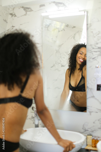 Back view black happy girl looking at mirror reflection in bathroom.