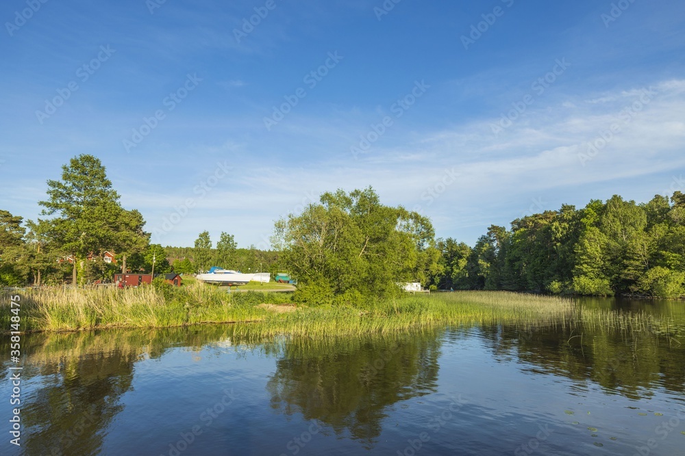 Beautiful nature landscape view of lake and motor boat parked on coast. Green trees and plants on blue sky with white clouds background. Sweden. Europe.
