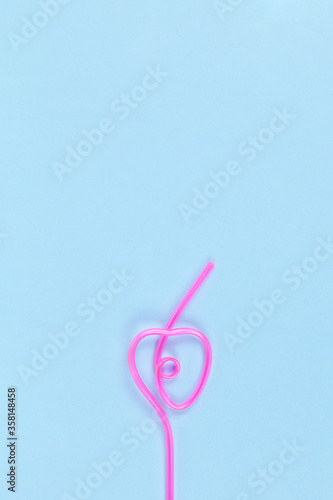 Disposable curly plastic pink straw for drinks in shape of heart on pastel blue background, copy space. Festive concept, party, birthday. Flat lay, top view. Vertical. For social media © AllUneed