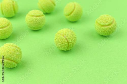 Chewing gum in the shape of a tennis ball on the green background. Harm to teeth. Place for text.