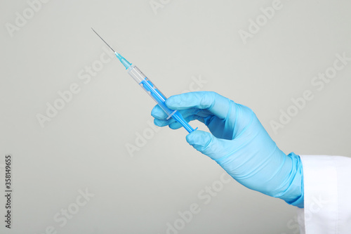 Doctor hand in glove holding syringe on grey background