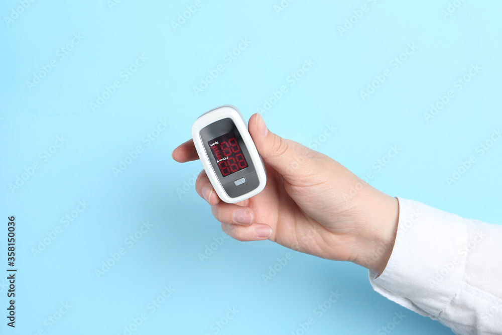 Woman holding modern fingertip pulse oximeter on light blue background, closeup Woman holding modern fingertip pulse oximeter on light blue background, closeup