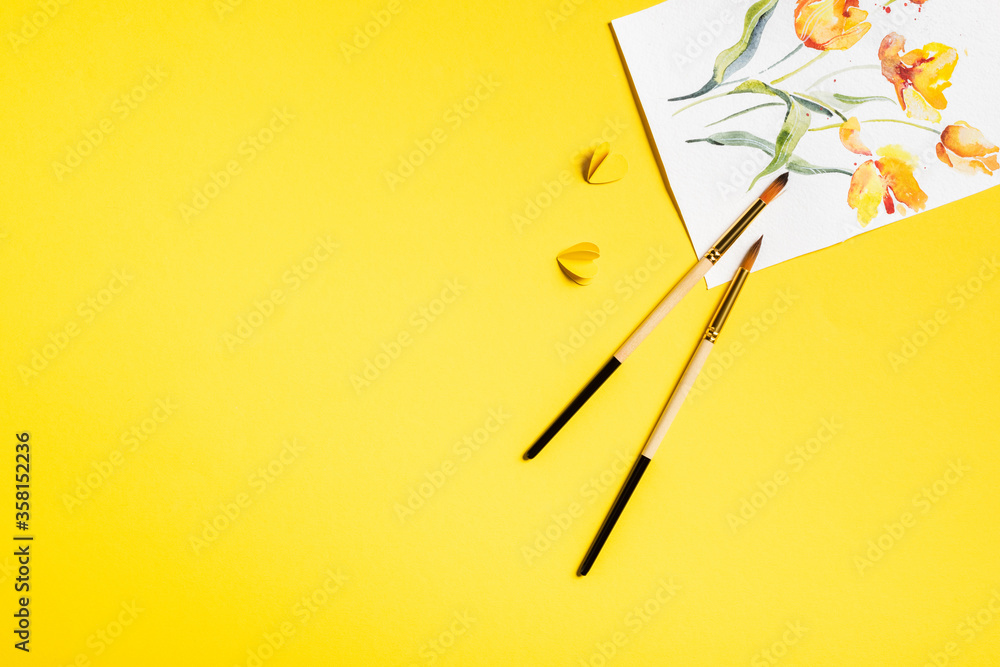 top view of paintbrushes near drawn flowers on painting and paper cut elements on yellow top view of paintbrushes near drawn flowers on painting and paper cut elements on yellow